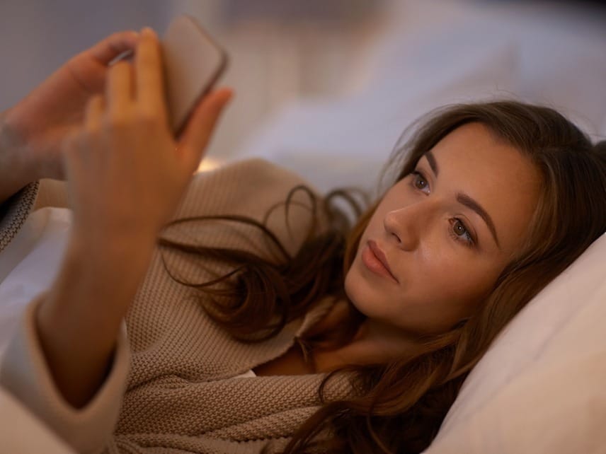 A woman sitting on a couch checking her phone while waiting for a response to an apology text sent to her boyfriend.