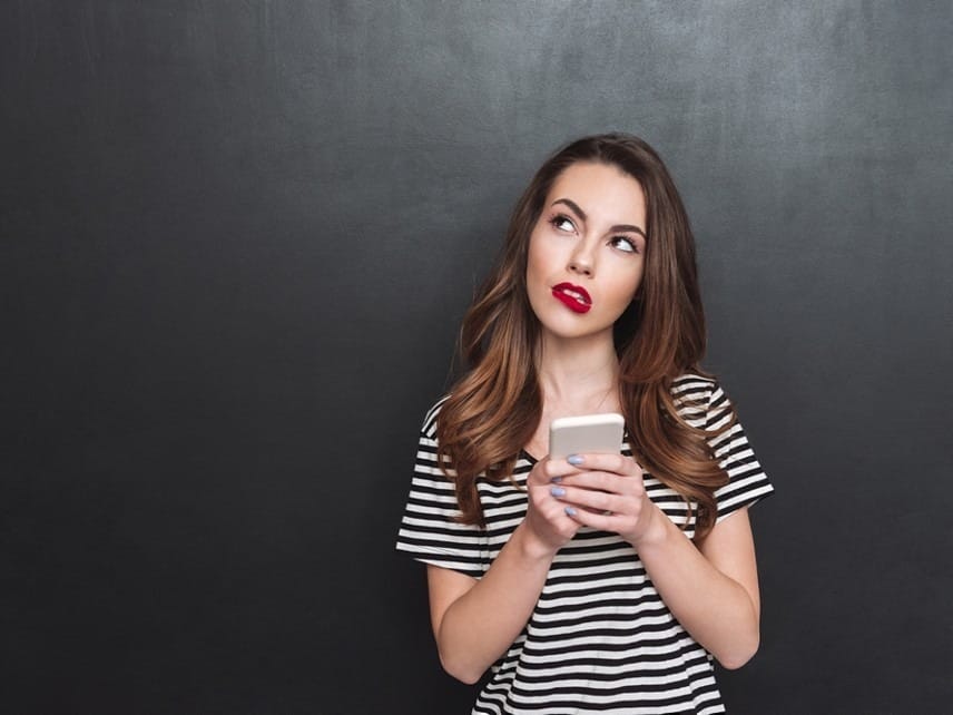 A thoughtful woman holding her phone while standing, practicing healthy relationship communication boundaries