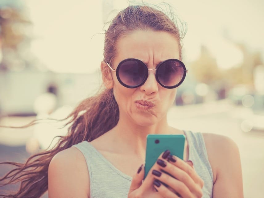 A woman walking outside while holding her smartphone and sending a message to her partner at a bad time, illustrating text timing issues in a relationship