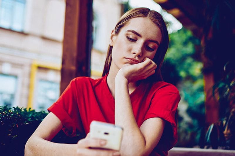 A woman sitting down and holding her smartphone, looking at a text message on the screen from her partner that says sorry I was busy